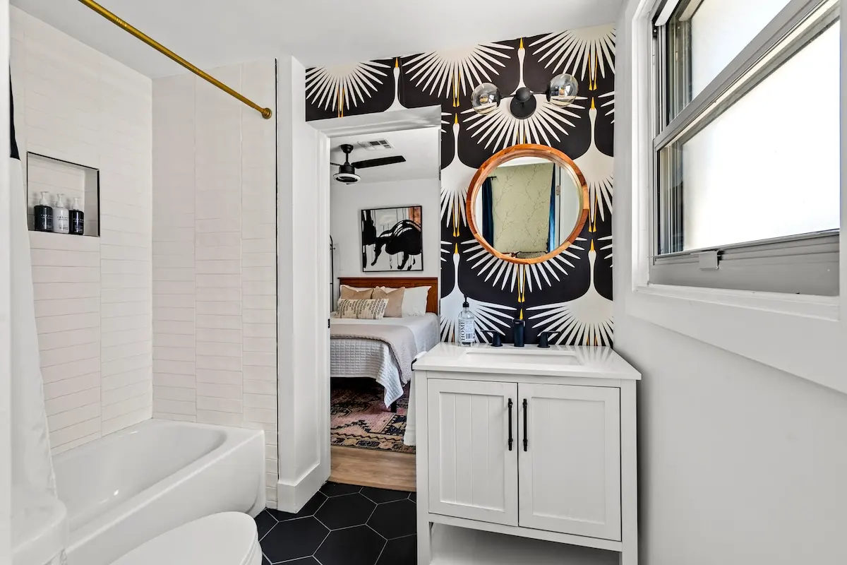 Serving bold glam energy! This guest-favorite bathroom features graphic wallpaper, modern lighting, and a peek into one of our cozy bedrooms.